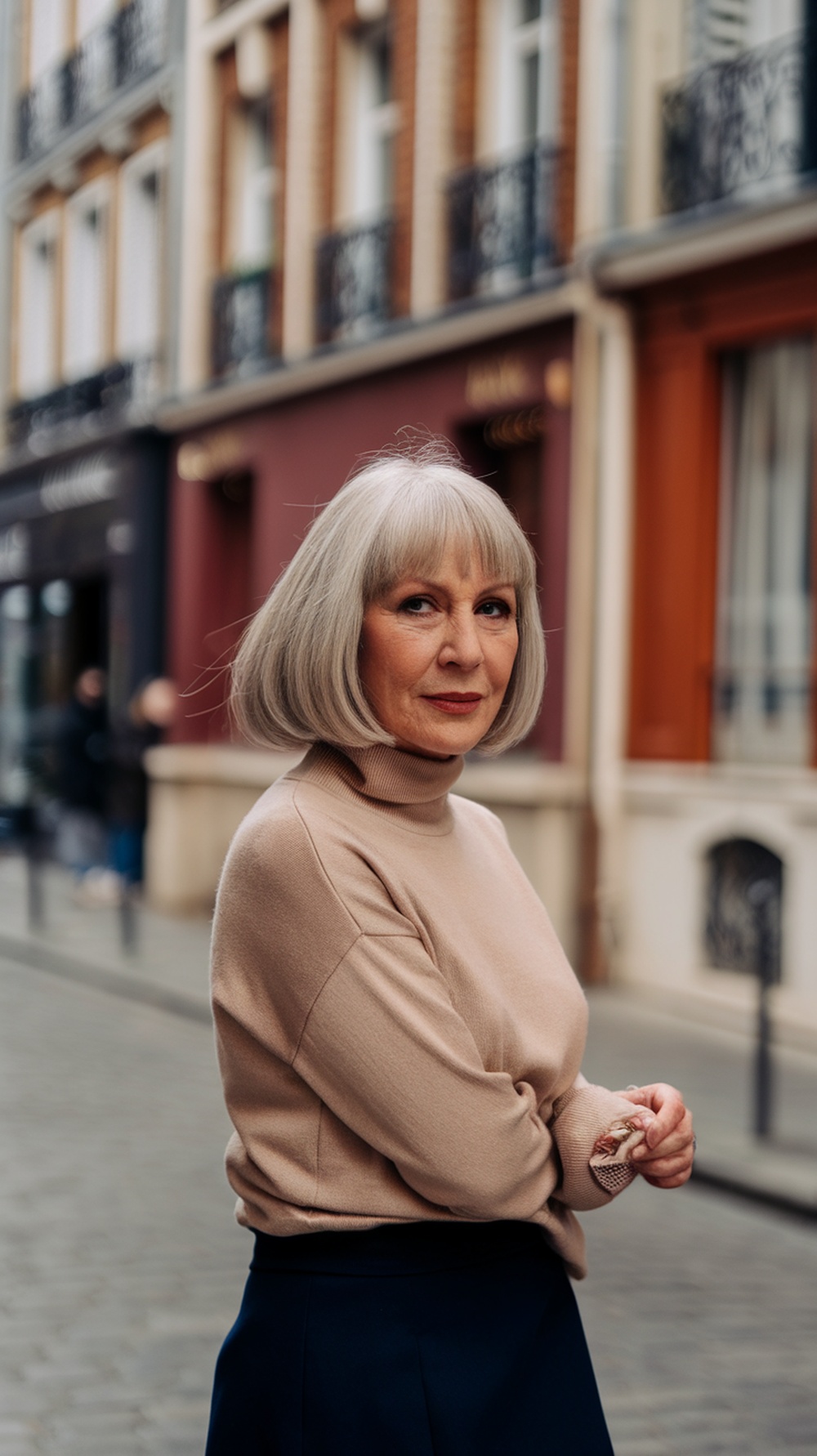 Woman with a classic French bob hairstyle, wearing a beige sweater, standing in a Parisian street.