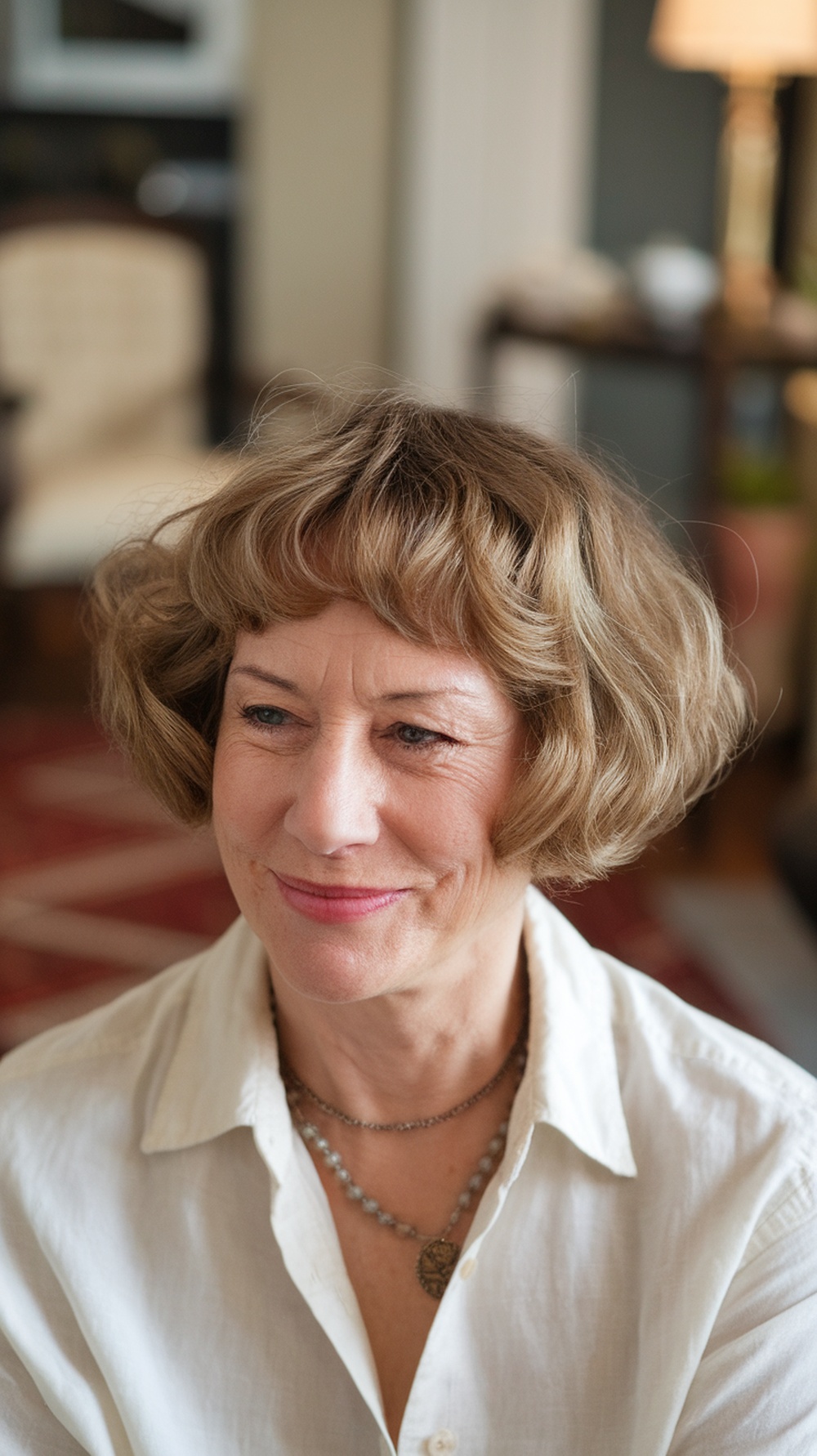 A woman with a soft curly bob hairstyle, wearing a white blouse and jewelry, smiling warmly.