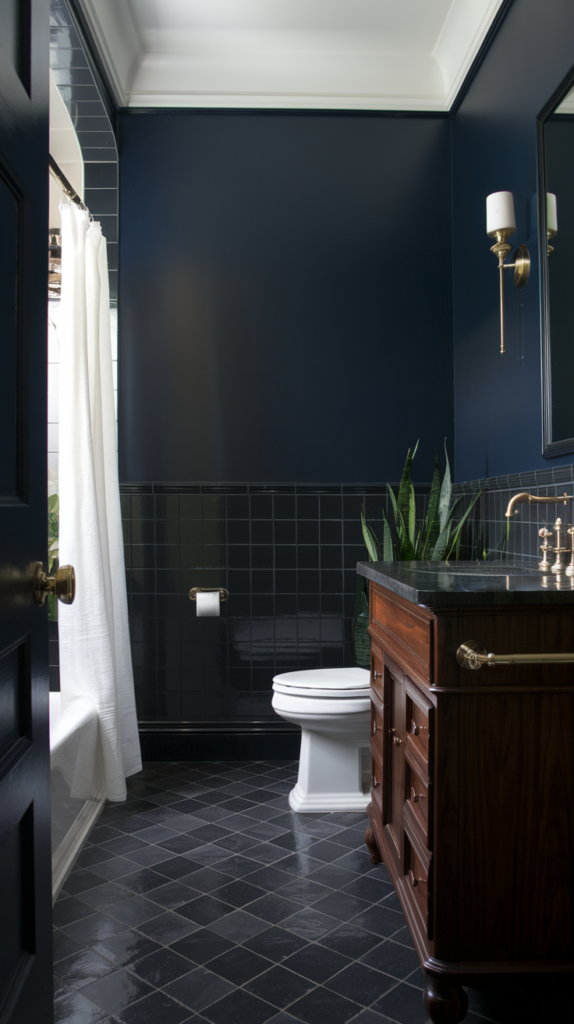 A photo of a bathroom with dark and bold colors. The wall is painted in a deep navy blue color. The floor is made of dark grey tiles. The vanity is made of a dark wood. The fixtures, such as the faucet and the light switch, are in a shiny brass color. The room contains a white toilet and a white shower curtain. There is a potted plant near the window.