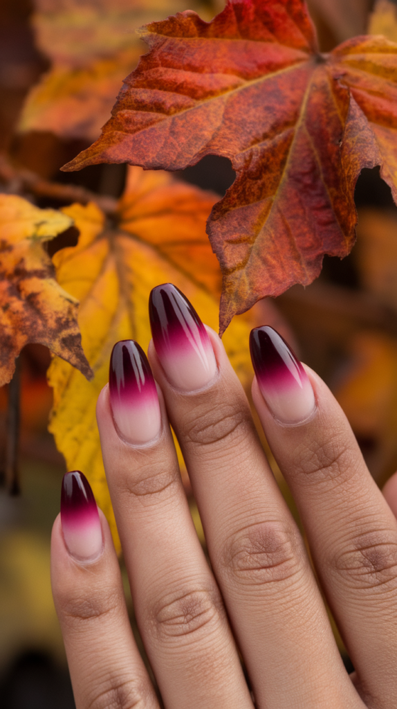 Close-up of a hand with warm burgundy ombre nails against autumn leaves